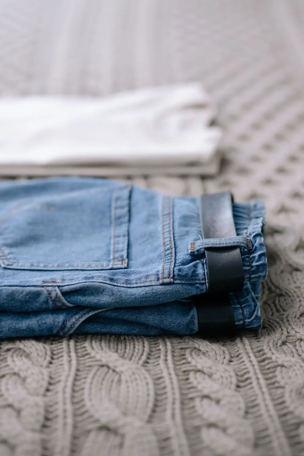Reference photo 3: folded jeans with a belt on a knit blanket — jeans we manufacture and export in bulk to South Africa